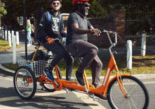 Two people riding an orange tandem trike