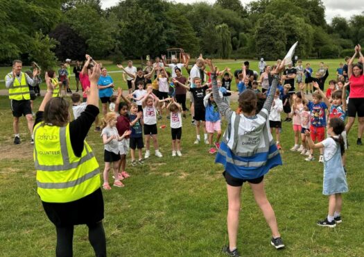 crowd of children jumping and clapping in a park before junior parkrun starts